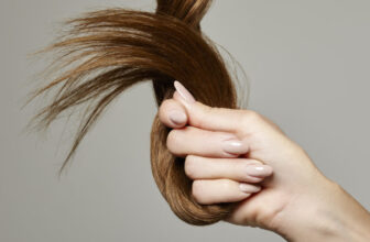 Woman holding hair against a gray background.