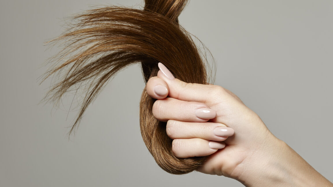 Woman holding hair against a gray background.