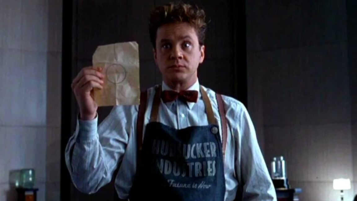 goofy looking man in 1950s mailroom apron holding up a piece of paper with a circle drawn on it